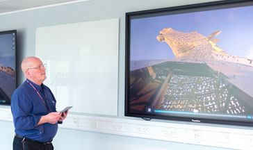 A ҹɫֱ staff member standing by 2 screens showing the Scottish Kelpies sculpture