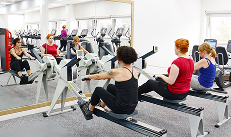 A row of women using rowing machines in front of a mirrored wall, ҹɫֱ