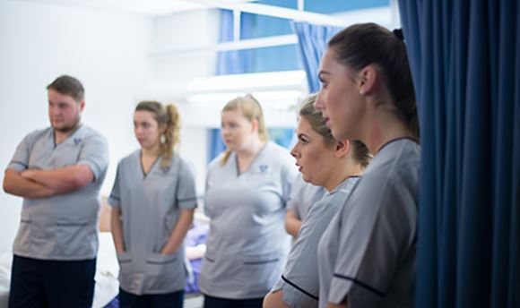 A row of ҹɫֱ student nurses listening intently as a senior nurse speaks to them