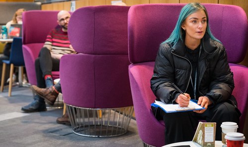 Student with vibrant blue hair sat on purple pod seat in ҹɫֱ Atrium